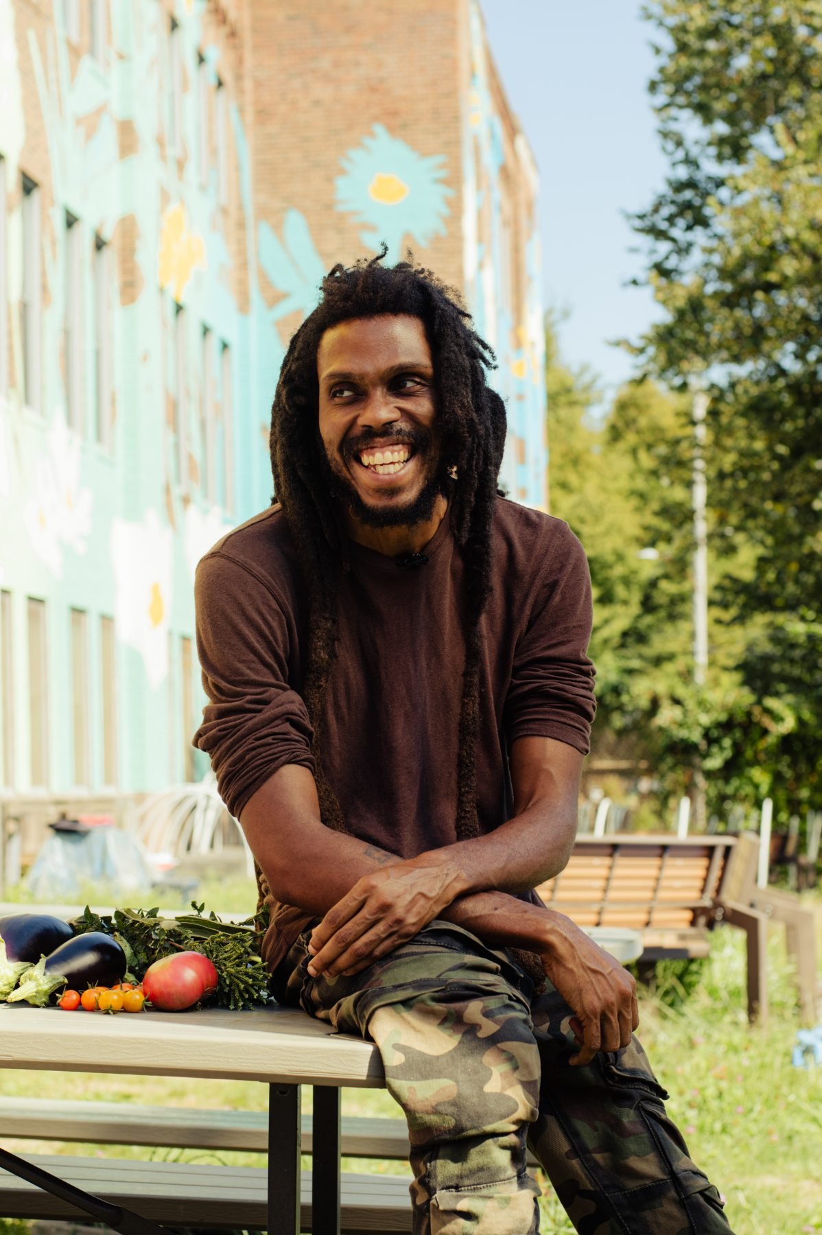 Farmer D at the Armory Community Garden, sitting beside the day&rsquo;s harvest with the mural wall behind him.